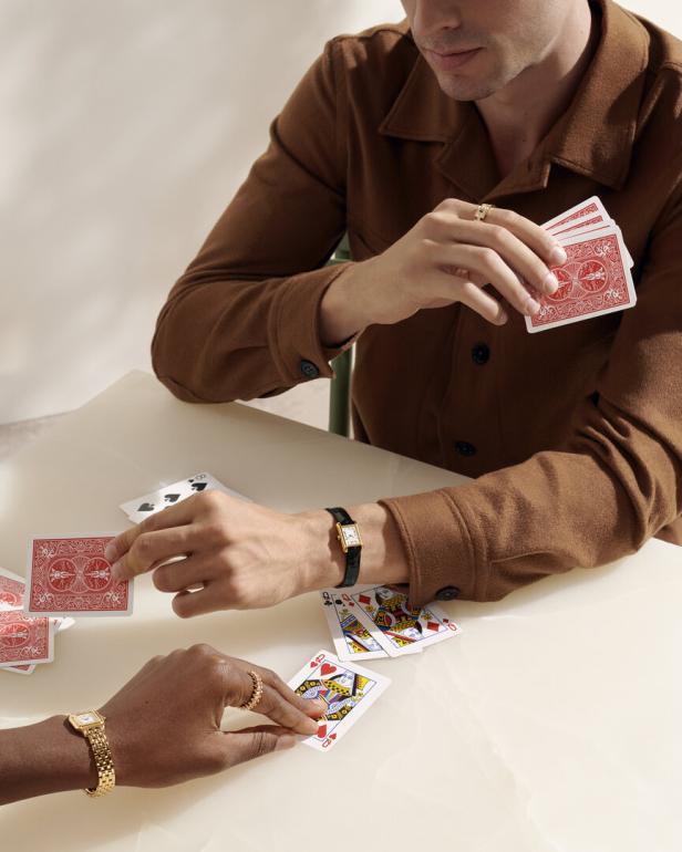Zwei Personen spielen Karten und tragen dabei Uhren und Ringe.