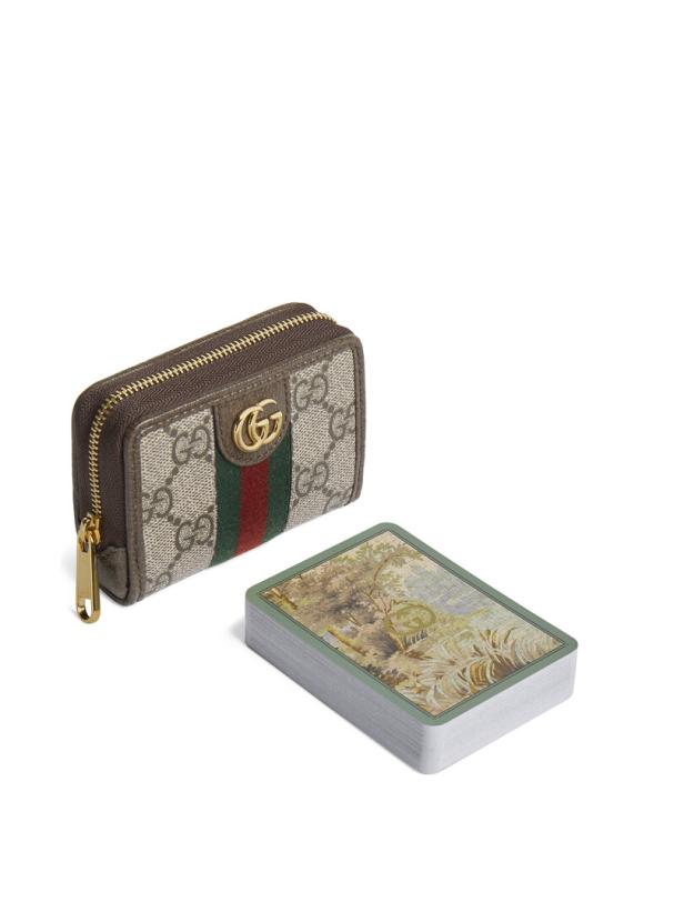Eine Gucci-Geldbörse mit Reißverschluss und ein Kartenspiel liegen auf einem weißen Hintergrund.