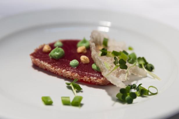Tuna Tataki mit grüner Soße und Kräutern auf einem Teller.