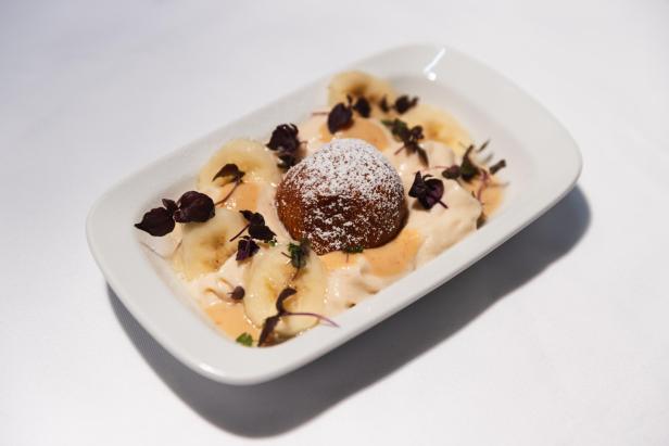 Ein Dessertteller mit einem Puderzucker-bedeckten Ball, Bananenscheiben und Creme.
