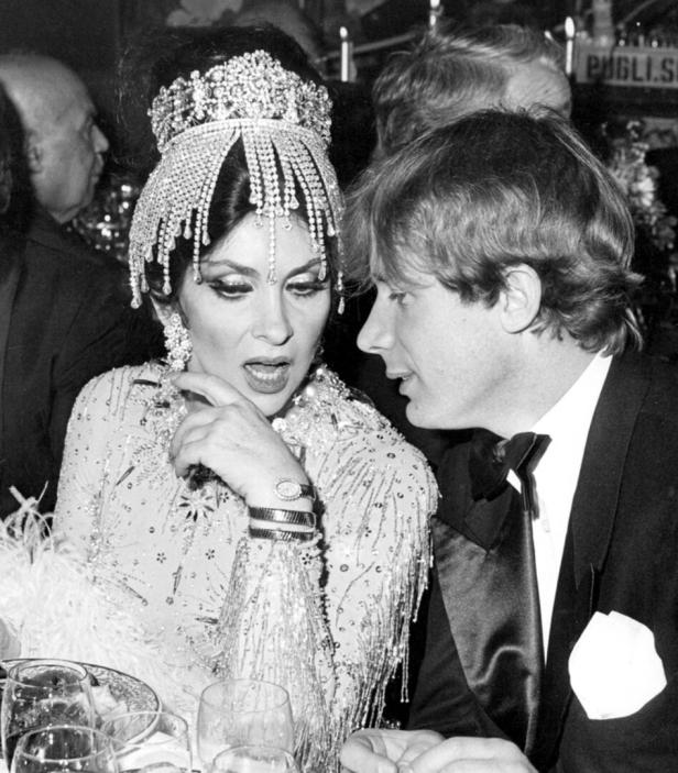 Gina Lollobrigida mit einem Mann bei einer Veranstaltung, gekleidet in ein aufwendiges, glitzerndes Kleid und Diadem.