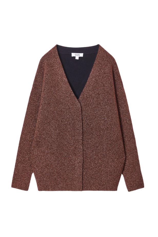 Eine glitzernde, kastanienbraune Strickjacke der Marke COS vor einem weißen Hintergrund.