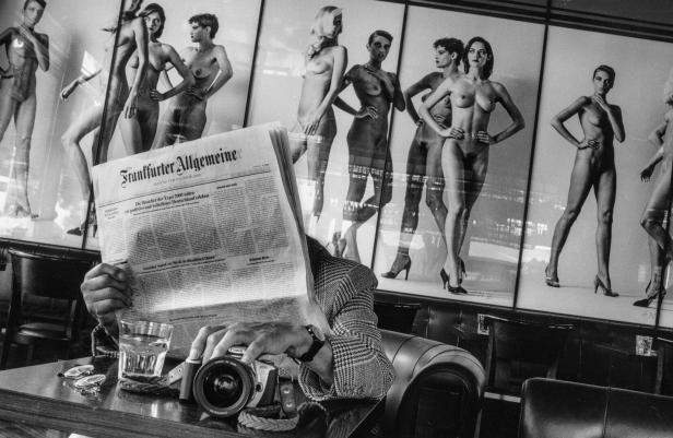 Eine Person liest die Frankfurter Allgemeine Zeitung in einem Café, im Hintergrund Aktfotografien.