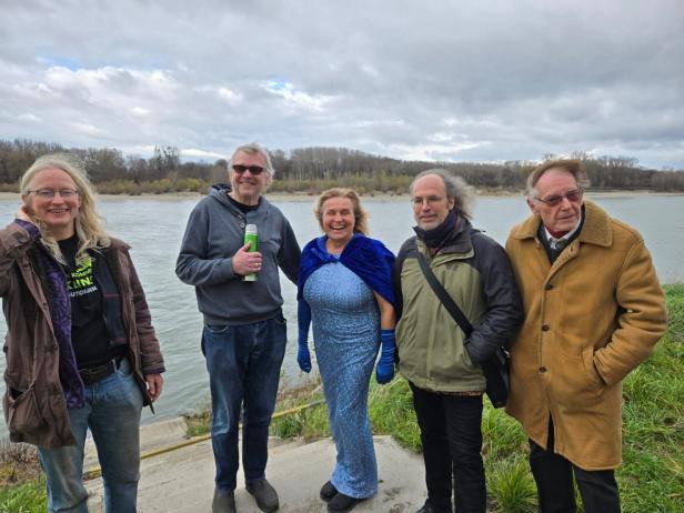 Fünf ehemalige Aubesetzer stehen am Donauufer. Der Wind zerzaust ihnen die Haare. Im Hintergrund fließt die Donau