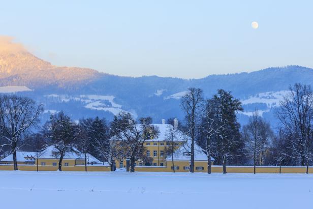 Das Schloss Frohnburg im Winter mit schneebedeckten Feldern und Bergen im Hintergrund.