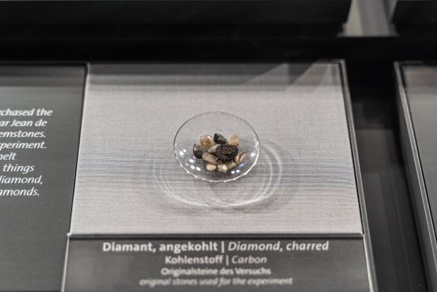 Eine kleine Glasschüssel, in der verkohlte Diamantstücke liegen, die aussehen wie Kieselsteine.