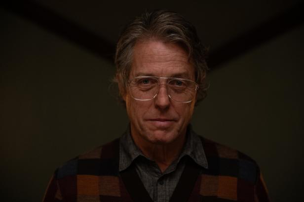 Ein Porträt von Hugh Grant mit Brille und karierter Strickjacke.