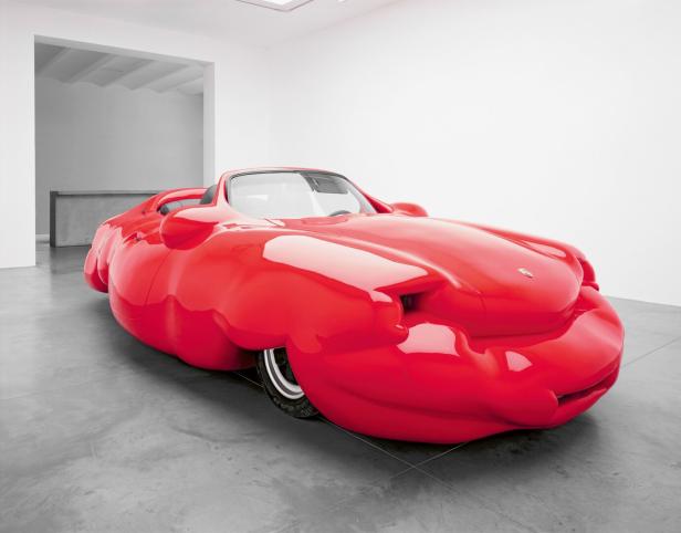 Ein aufgeblähtes, rotes Porsche-Cabriolet steht in einem Ausstellungsraum.