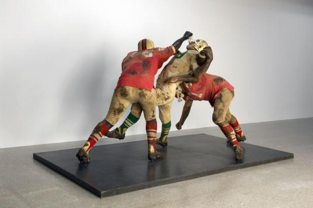 Eine Skulptur von drei schmutzigen American-Football-Spielern in Aktion.