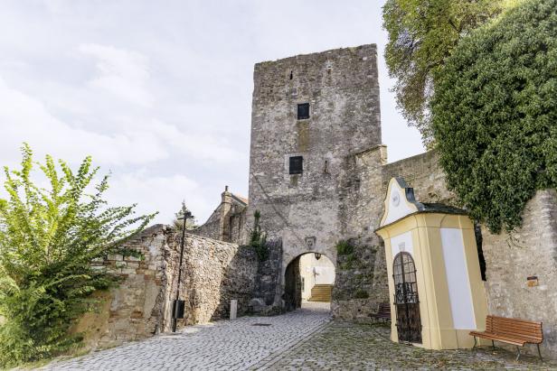 Ein mittelalterlicher Turm und eine Kapelle säumen einen gepflasterten Weg.