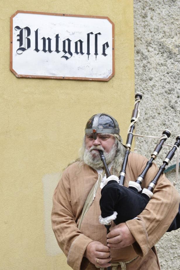 Ein Mann mit Wikingerhelm spielt Dudelsack vor einem Schild mit der Aufschrift „Blutgasse“.