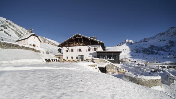 Ein Berghotel und eine kleine Kirche in einer verschneiten Winterlandschaft.