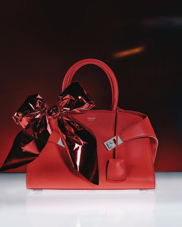 Eine rote Ferragamo-Handtasche mit einer glänzenden, roten Schleife vor einem roten Hintergrund.