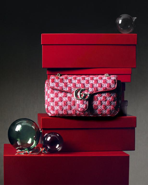 Eine rosafarbene Gucci-Tasche liegt auf einem Stapel roter Geschenkboxen, dekoriert mit Weihnachtskugeln.