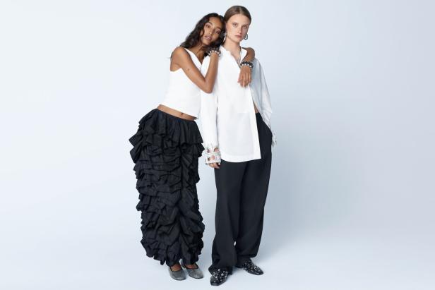Zwei Models posieren in weißer und schwarzer Kleidung vor einem hellen Hintergrund.