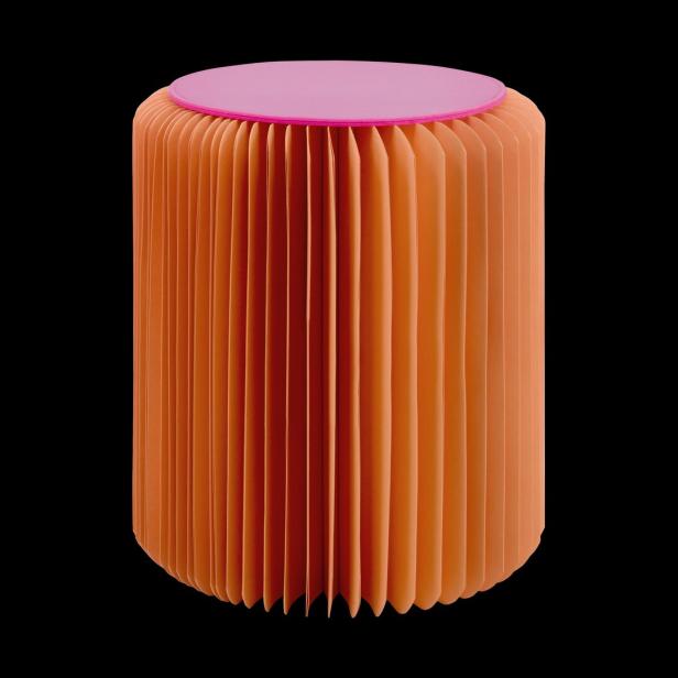 Ein orangefarbener Papierhocker mit einer pinkfarbenen Sitzfläche vor einem schwarzen Hintergrund.