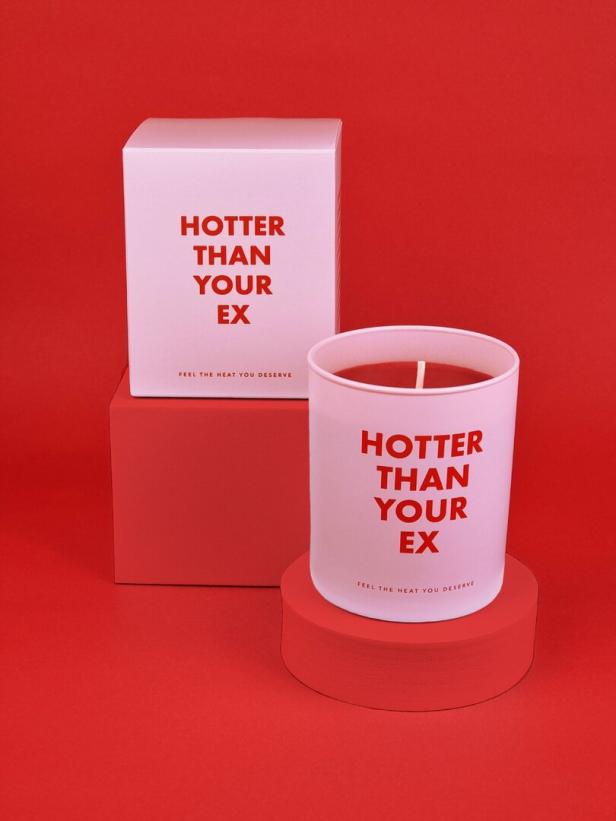 Eine Kerze und ihre Verpackung mit der Aufschrift „Hotter Than Your Ex“ vor rotem Hintergrund.