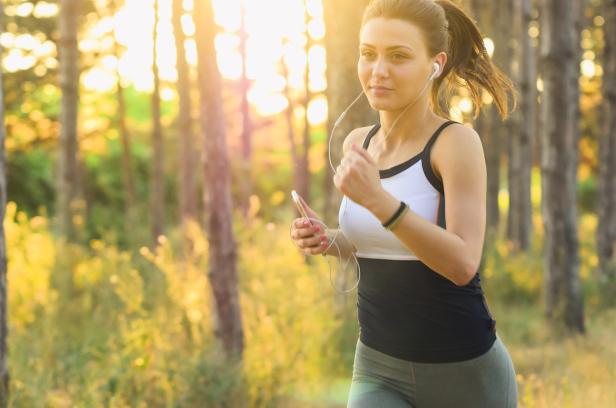 Eine Frau mit Kopfhörern joggt durch den Wald.