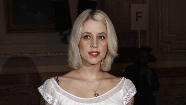 Eine Frau mit blonden Haaren und einem Nasenring trägt ein weißes Oberteil.