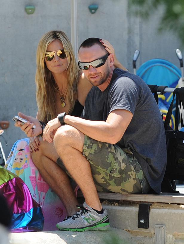 Heidi Klum sitzt mit einem Mann im Freien, sie schaut auf ihr Handy.