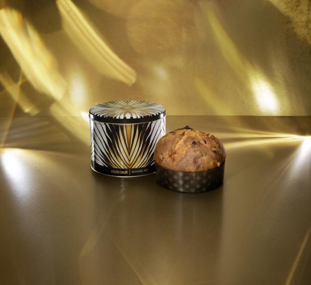 Ein Panettone neben einer dekorativen Dose von Roberto Cavalli auf einem goldenen Untergrund.