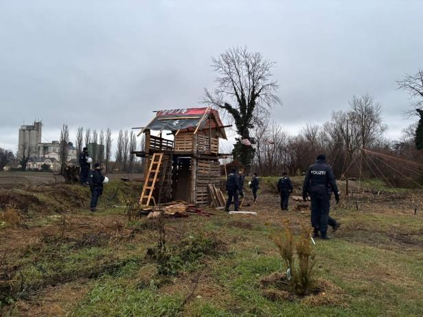 Polizisten stehen vor einem Baumhaus aus Paletten auf einem Feld.