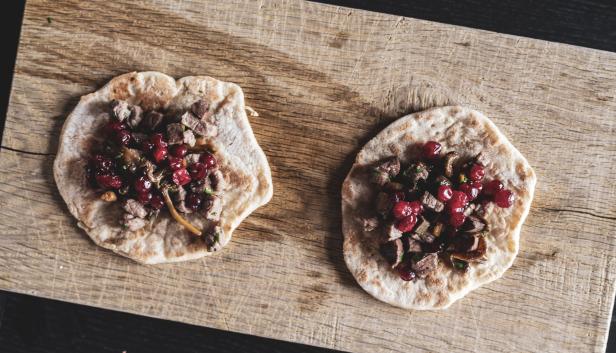 Zwei Fladenbrote belegt mit Fleisch, Preiselbeeren und Kräutern auf einem Holzbrett.
