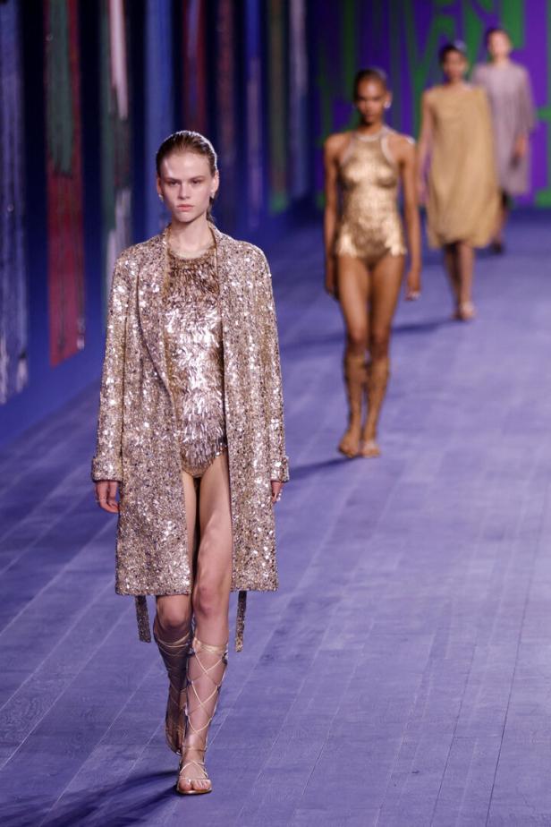 Eine Frau in einem goldenen Outfit und Gladiatorensandalen auf dem Laufsteg.