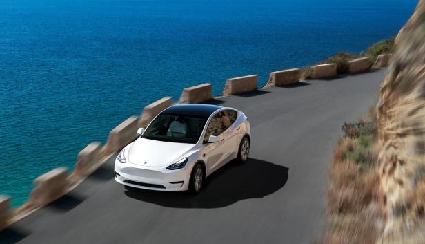 Das Tesla Model Y fährt auf einer Küstenstraße entlang.