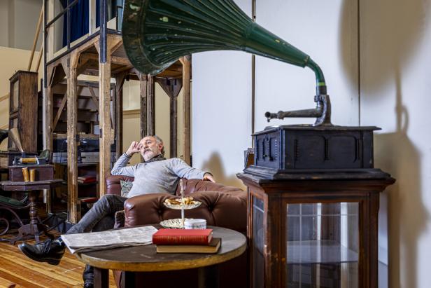 Karl Markovics sitzt entspannt auf einem Chesterfield-Sofa, ein Teil der Kulisse.