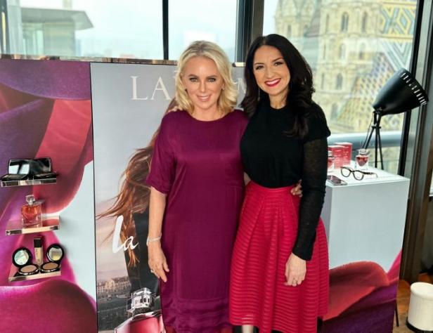 Zwei Frauen posieren vor einem Werbeplakat für ein Lancôme-Parfüm.