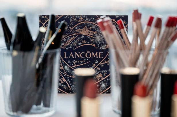 Ein Lancôme-Adventskalender umgeben von Make-up-Produkten in Gläsern.