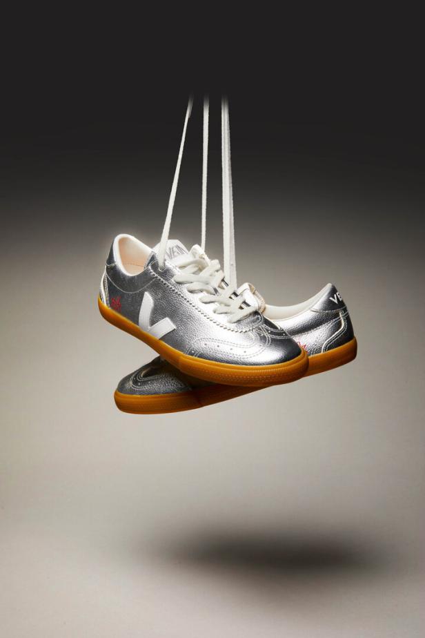 Ein Paar silberne Veja-Sneakers hängen an ihren Schnürsenkeln.