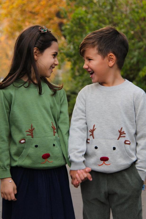 Ein Mädchen und ein Junge halten Händchen und tragen Pullover mit Rentier-Applikationen.