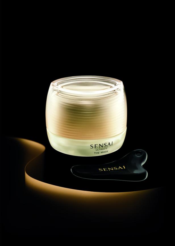 Ein Tiegel „Sensai Ultimate The Mask“ und ein schwarzer Gua Sha Stein auf einer glänzenden Oberfläche.