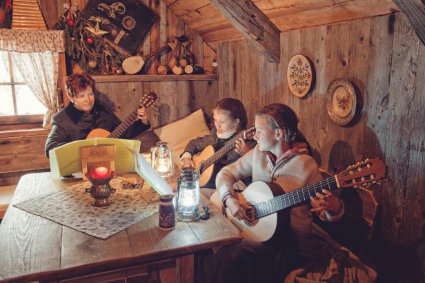 Drei Personen spielen Gitarre in einer gemütlichen Holzhütte.