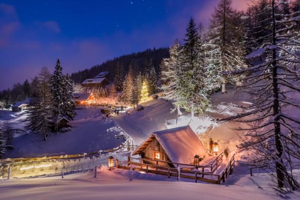 Eine verschneite Hütte ist nachts von Laternen beleuchtet.