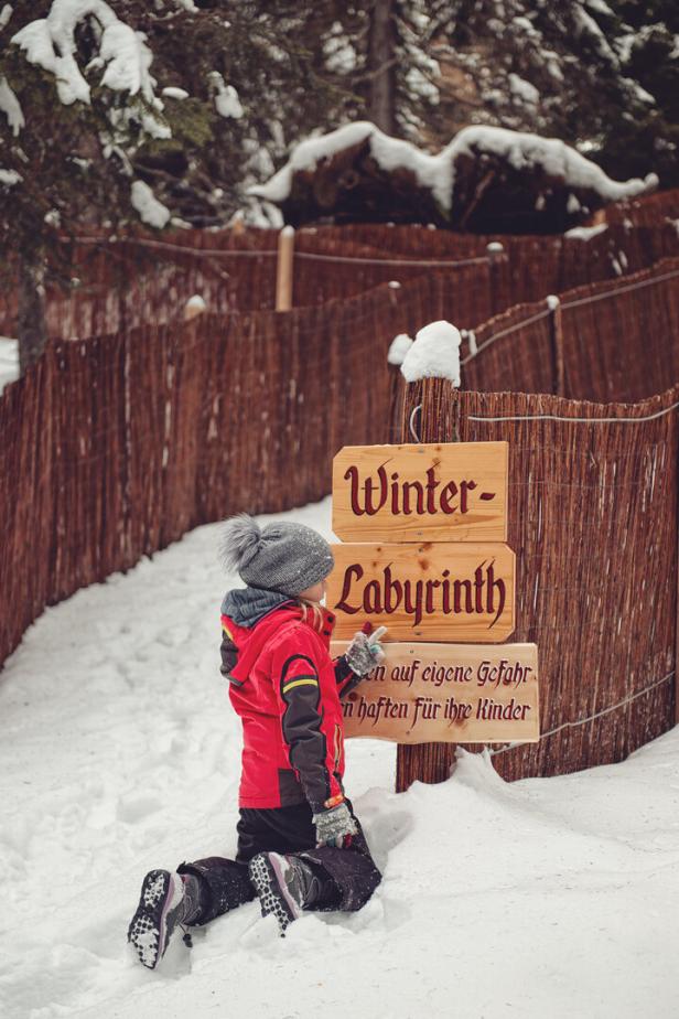 Ein Kind kniet im Schnee vor dem Eingang zum „Winter-Labyrinth“.