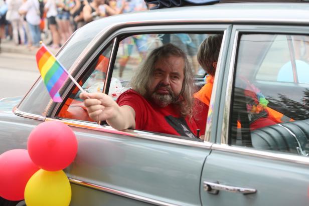 Ein Mann hält eine Regenbogenflagge aus dem Fenster eines Oldtimers.