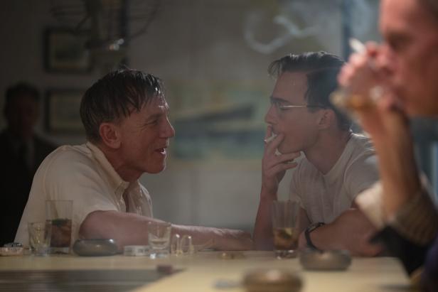 Daniel Craig und ein junger Mann sitzen an einem Tisch und rauchen Zigaretten.