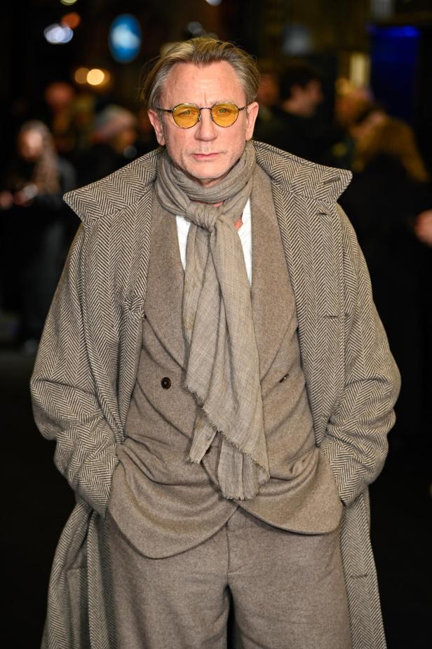 Daniel Craig trägt einen Mantel, einen Anzug und eine gelbe Brille.