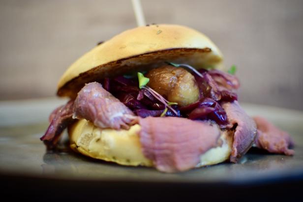 Ein Burger mit Fleisch, Rotkohl und einer Marone auf einem Teller.