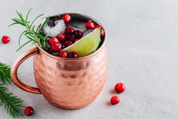 Ein Getränk in einem Kupferbecher mit Eis, Cranberries, Limette und Rosmarin garniert.