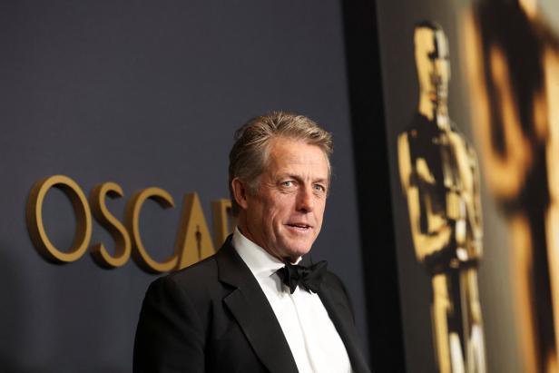 Hugh Grant posiert vor dem Oscar-Logo.