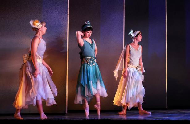 Drei Ballerinen in farbenfrohen Kleidern stehen auf einer Bühne.