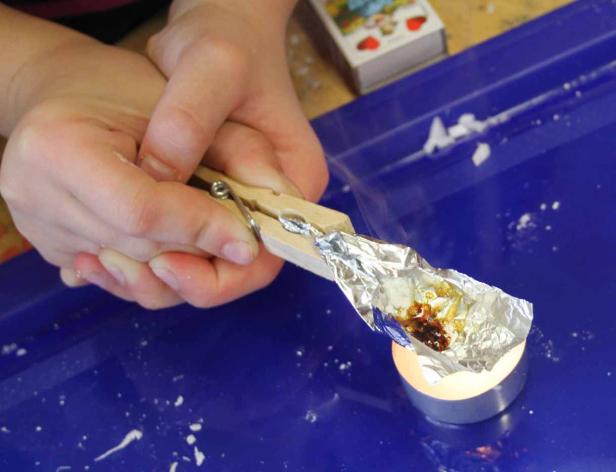 Eine Person erhitzt mit einer Kerze und einer Wäscheklammer eine Substanz in Alufolie.