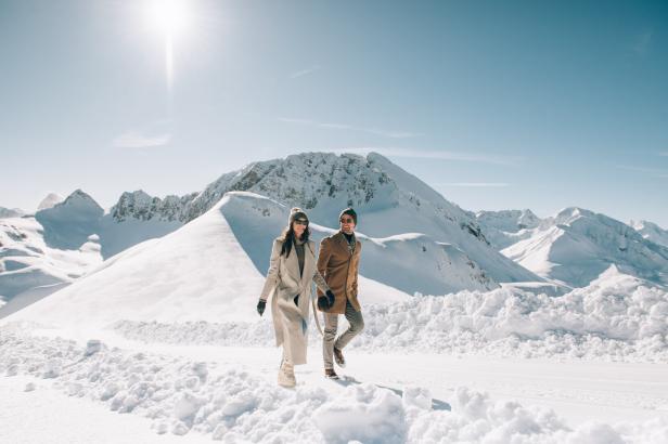 Ein Paar spaziert Hand in Hand durch eine verschneite Berglandschaft.