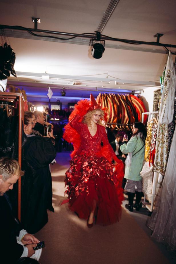 Eine Frau in einem roten, extravaganten Kleid mit Federn und passendem Hut.