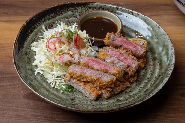 Ein Teller mit geschnittenem Rindfleisch-Katsu, Krautsalat und einer Schale mit Dip-Sauce.
