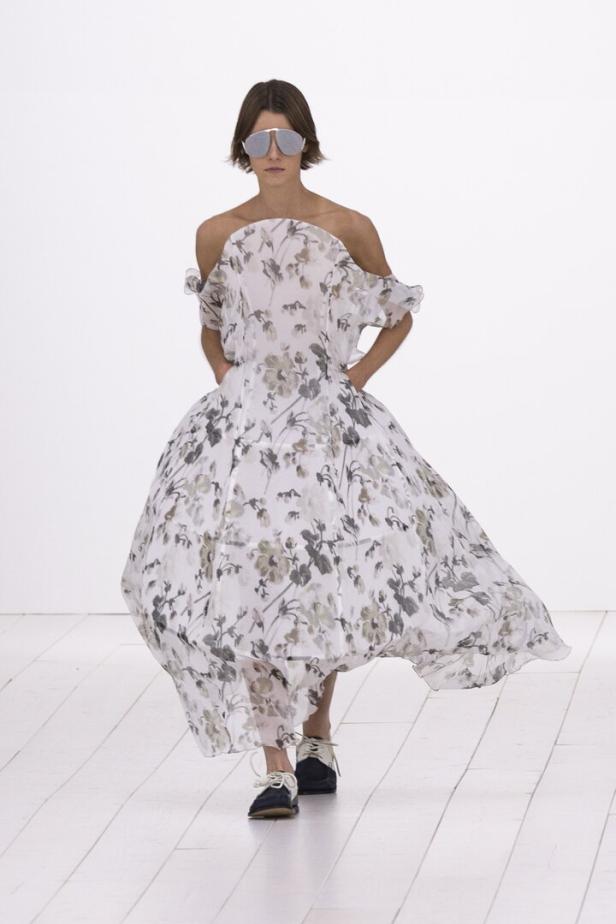 Eine Frau mit Sonnenbrille trägt ein schulterfreies, blumengemustertes Kleid.